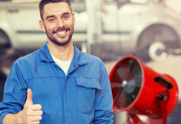 A man smiling giving a thumbs up with a red fan in the background.