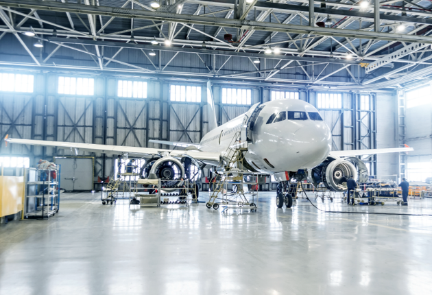 A well-lit airplane hangar with a man working on a commercial airplane.